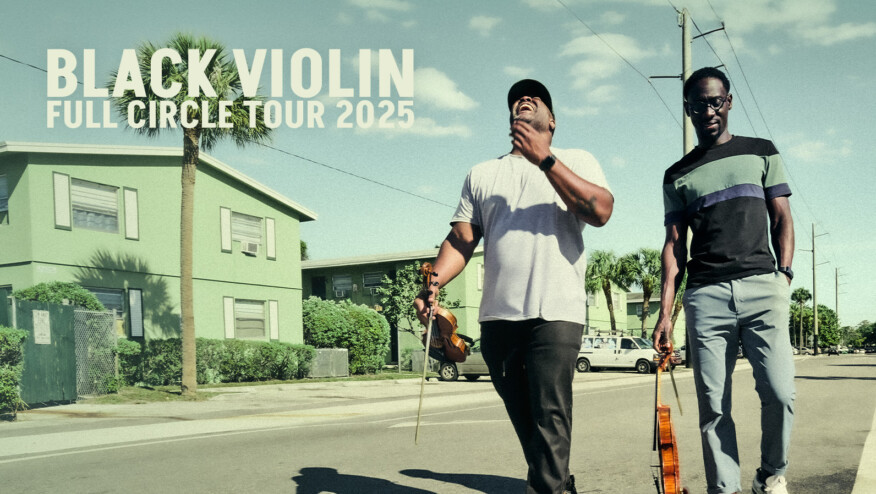 Two men walk on a street, both holding violins. Text reads, 