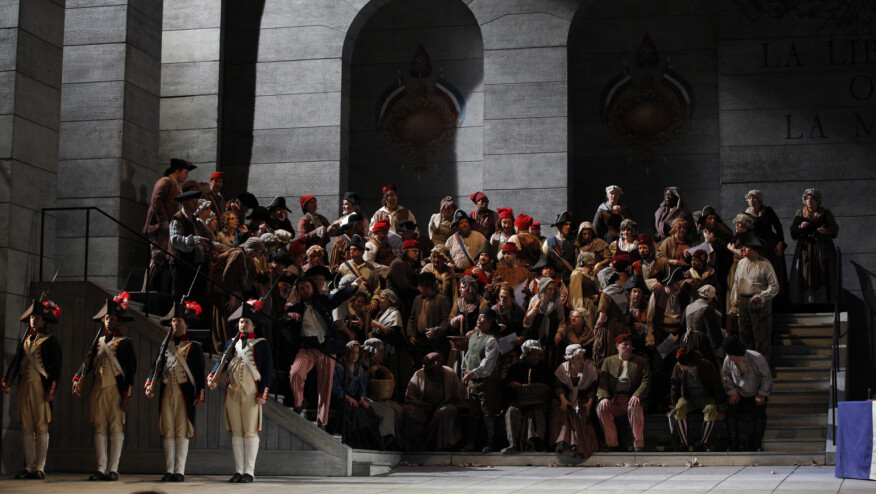 A group of townspeople sit on stairs with French soldiers in front.