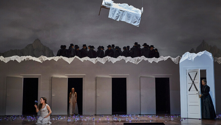 A bed hangs from the ceiling. Below it, a crowd of people in hats, open doors, and three women, one of which is holding a flower.