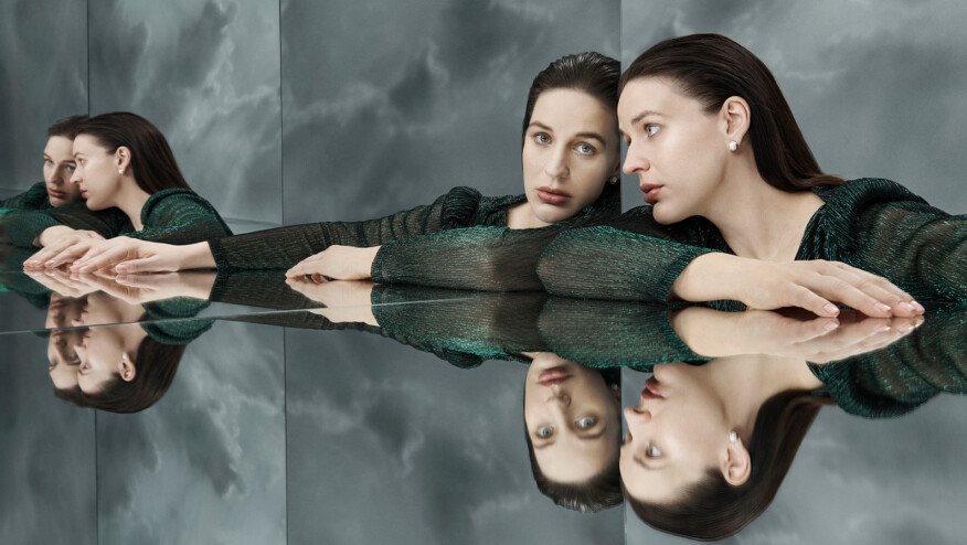A woman with slicked back hair looks into a mirror, with multiple reflections.