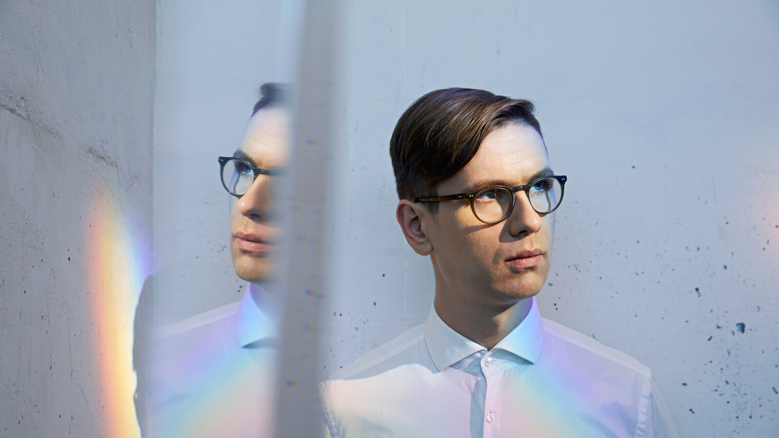 A man with glasses is reflected in a mirror. There is also a rainbow.