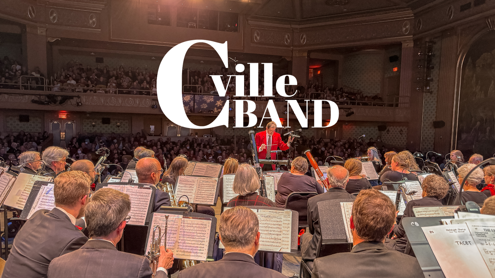 A man conducts a band, and a full audience is behind him. Text reads, 