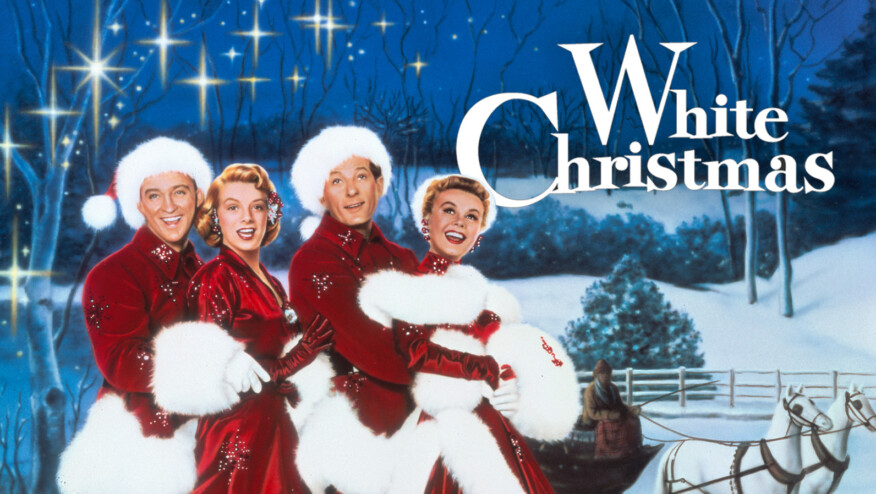 Four people in fur-lined Christmas outfits smile and sing in a winter scene. Text reads,