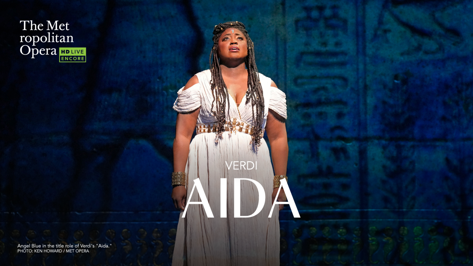 A woman in a white dress stands on a stage and sings, looking towards the ceiling. Text reads, 