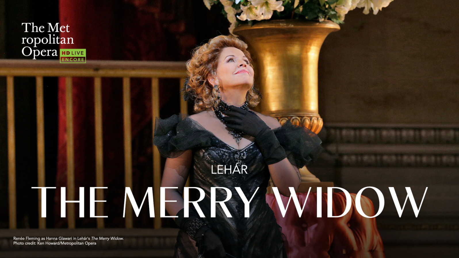 A woman in a black dress and gloves looks toward the sky ceiling while on a stage. Text reads, 