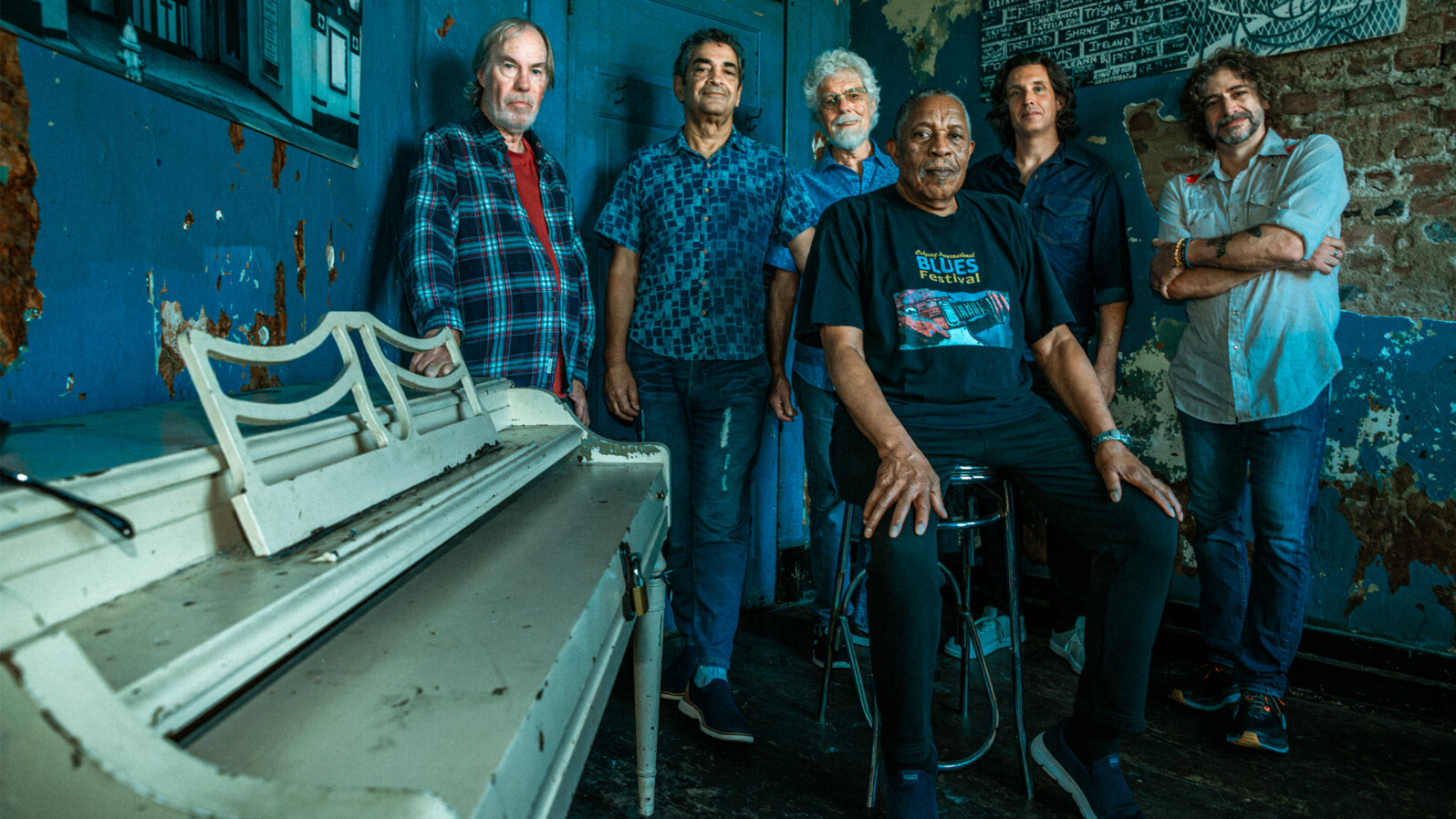 Six men pose in a room with a weathered piano.